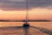 Sailboat gliding peacefully on the calm waters of Baía de Todos os Santos during sunset with vibrant orange and pink sky.