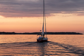 A sailboat gliding smoothly across calm waters under a fiery orange sunset.