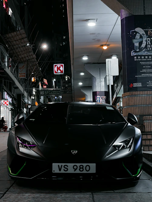 High-end Lamborghini parked under neon lights in a downtown setting.