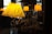A warm-lit cafe interior with decorative script lettering on a glass window that reads 'A Good Book Ending.' Several yellow lampshades hang above seating areas, casting a cozy ambiance.