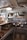 A kitchen area with various cooking utensils and equipment. Shelves hold cans labeled with ingredients like eggs, beets, and camel. Large ladles hang over metal countertops, and pots are stored below. Overhead, wiring is visible alongside a light fixture.