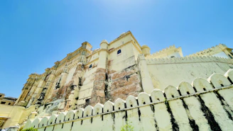 Majestic Rajasthan palace with golden sunlight highlighting intricate architecture under a clear blue sky.