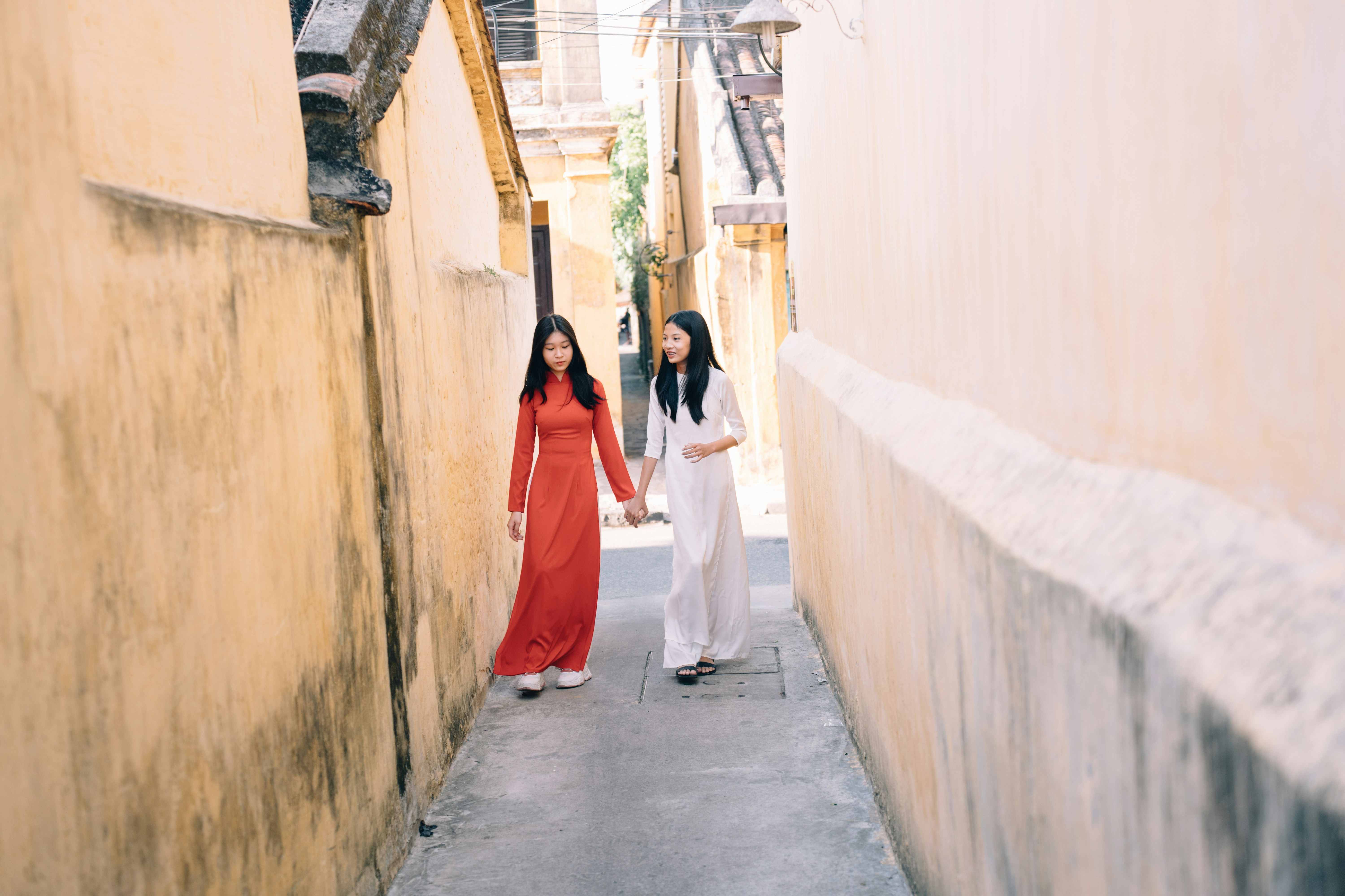 Two women in dresses walking down a narrow alley between buildings ...