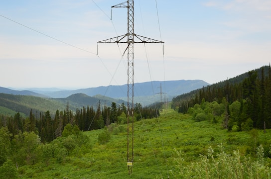 High-voltage transmission lines stretching across a green landscape towards a modern data center facility.