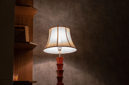 A fabric shade table lamp casting a gentle glow on a bedside table next to a stack of books.