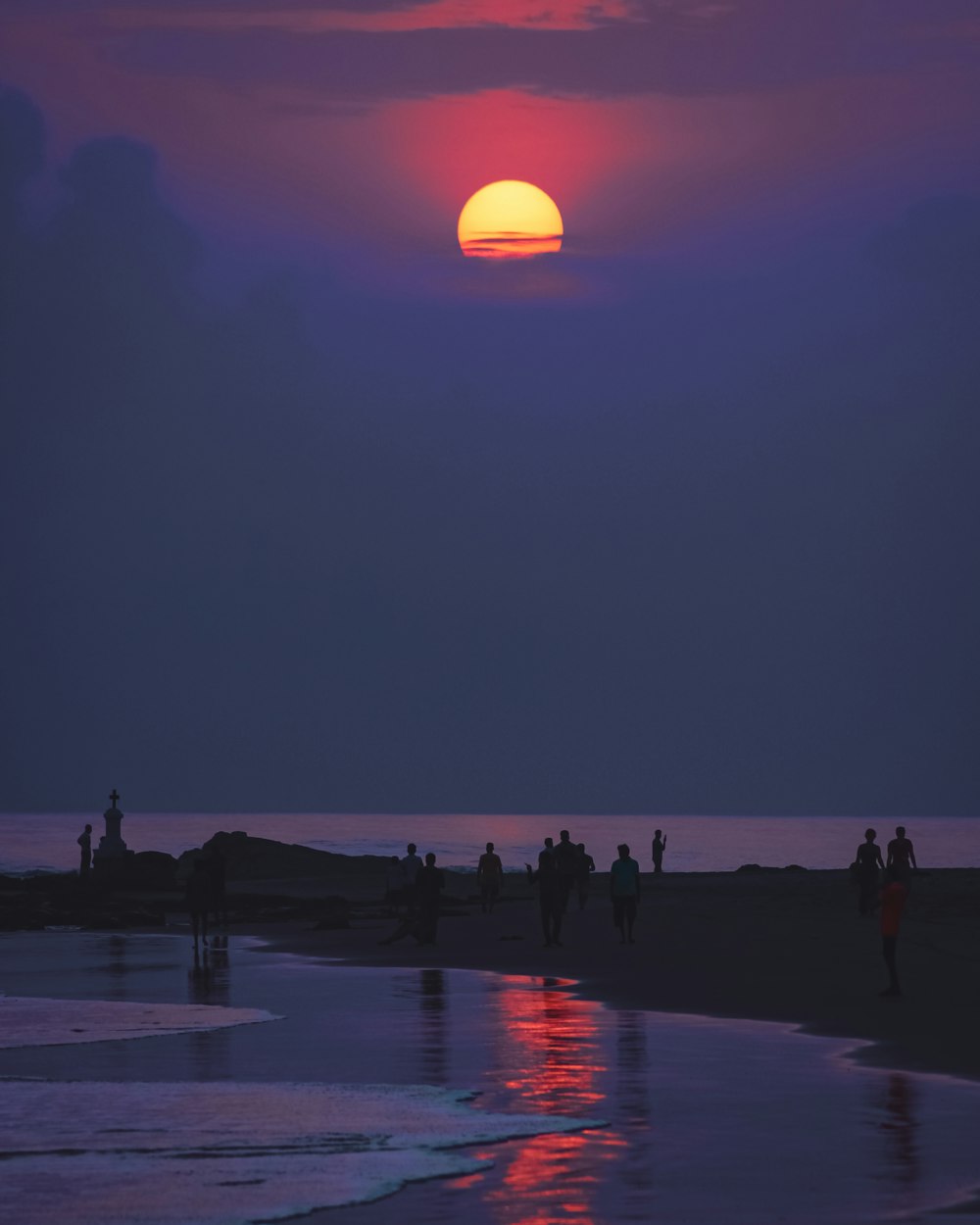 a group of people standing on a beach with the moon in the sky