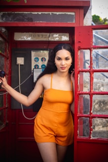 a woman posing in front of a red phone booth