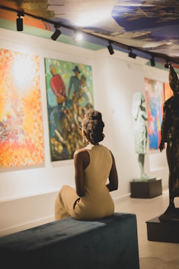 a statue of a person sitting on a couch in front of a wall of paintings