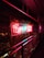 Neon sign in bright red and blue colors hangs prominently on a wall decorated with lush green ivy. The sign emits a warm glow that contrasts with the dark surroundings, creating a vibrant effect against the metal railing nearby.