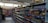A supermarket aisle filled with various packaged snacks and food items. Shelves on both sides are stocked with colorful bags and packets, including chips and canned goods. The lighting is bright, and the floor is tiled.