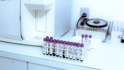 Equipamento automatizado de hemograma, tubos de coleta de sangue e um contador de tempo ao fundo