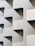 A building facade featuring an abstract, geometric design with repeating patterns of cut-out shapes. The structure is characterized by its minimalist aesthetic and uniform light-colored surfaces.