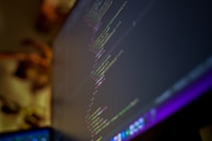 Close-up of hands typing on a keyboard with code on a monitor.