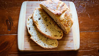 Freshly baked rustic bread loaf on a wooden cutting board with a linen cloth nearby.