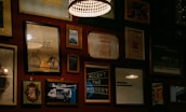 A wall adorned with various framed artworks and photographs, including images of a bicycle, inspirational quotes, and abstract designs. The lighting is warm and subtle, with a prominent hanging lamp creating a cozy atmosphere.