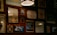 A wall adorned with various framed artworks and photographs, including images of a bicycle, inspirational quotes, and abstract designs. The lighting is warm and subtle, with a prominent hanging lamp creating a cozy atmosphere.