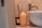 A beige ceramic aroma diffuser sits on a bathroom counter next to a dark brown candle jar labeled with text and a white ceramic vessel sink. The background features beige tiled walls.
