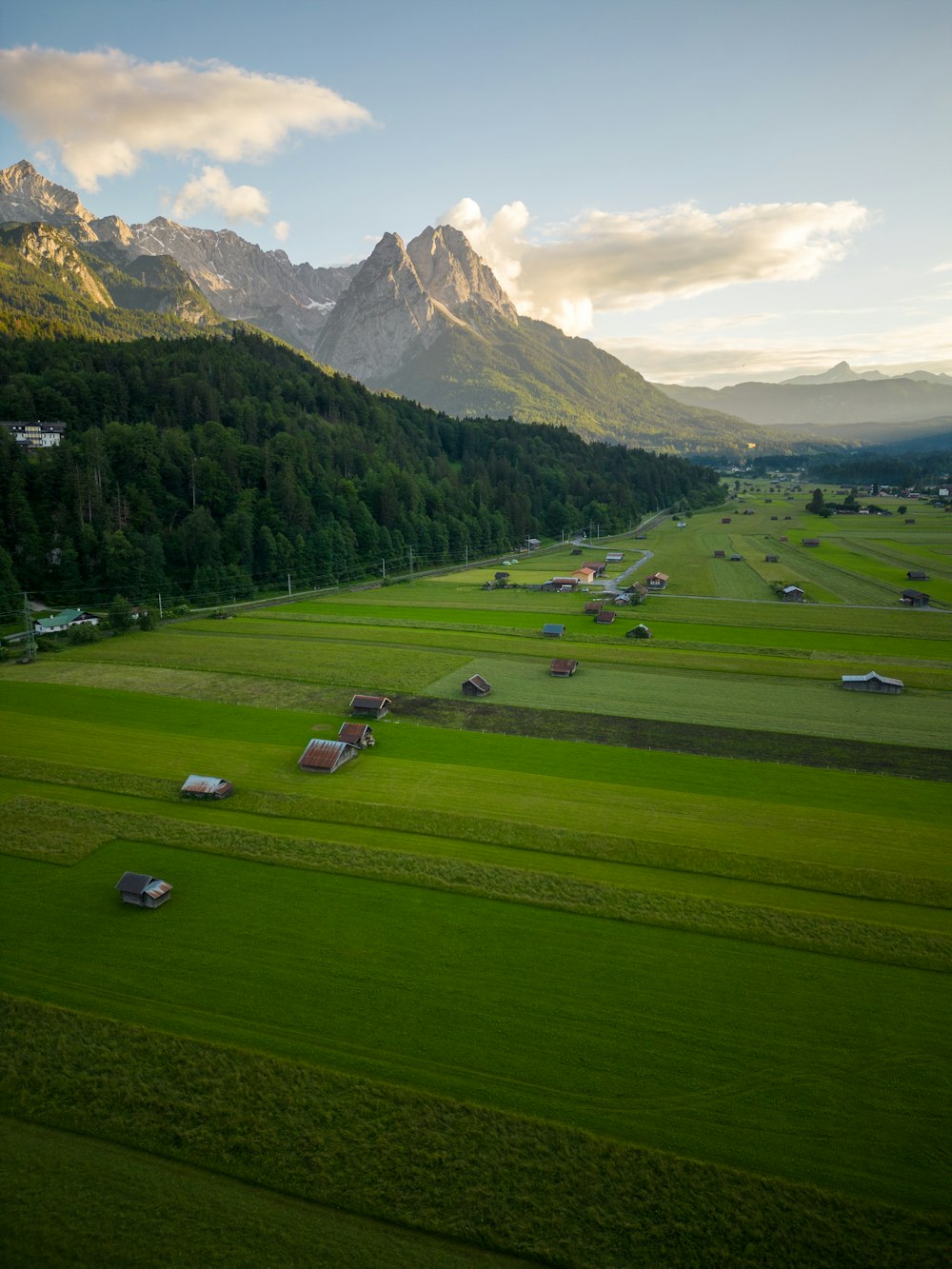 a large green landscape with houses and mountains in the background