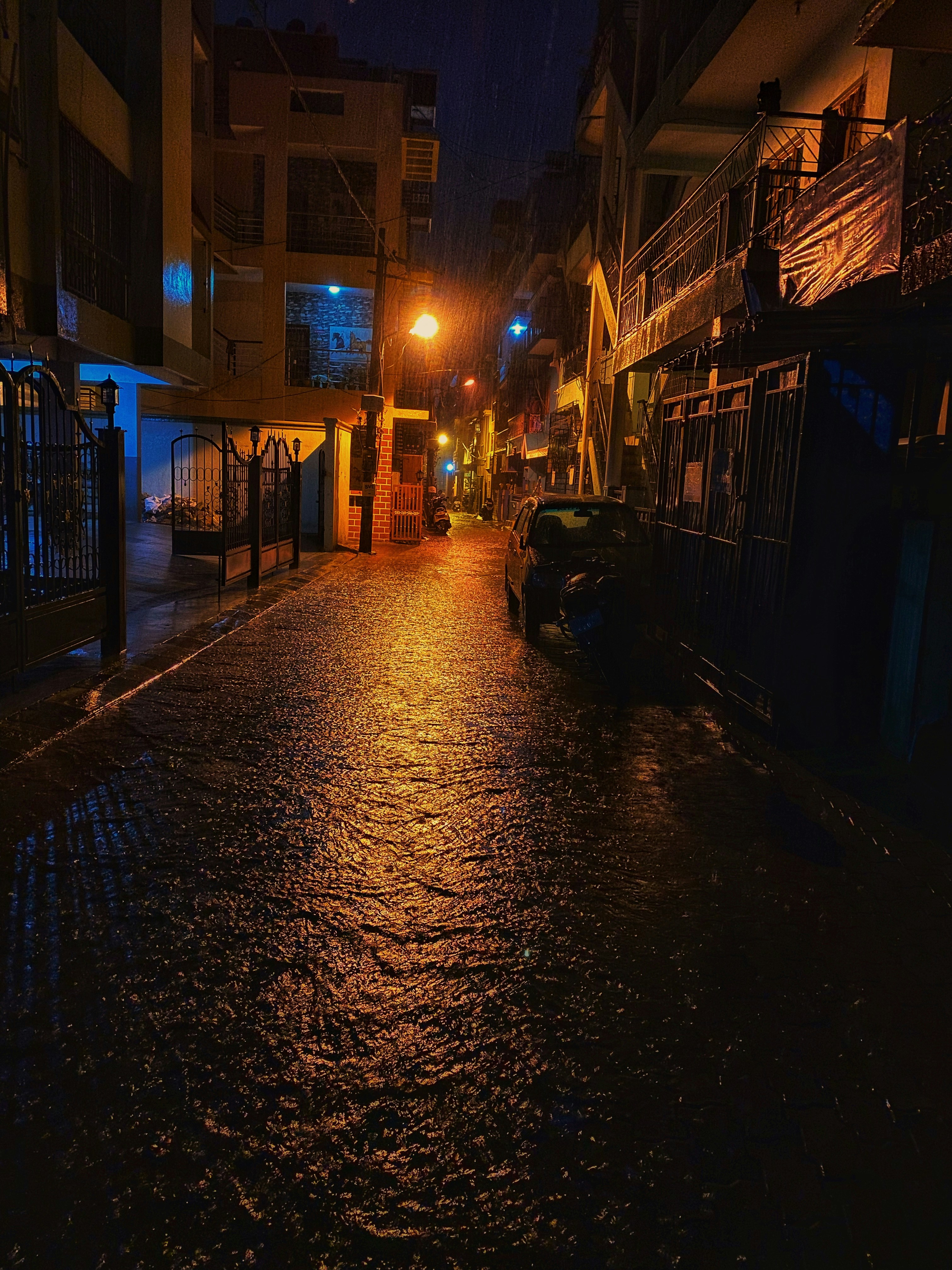 Dimly lit urban alley at night, wet pavement reflecting orange streetlights, dark brick walls, moody cinematic atmosphere