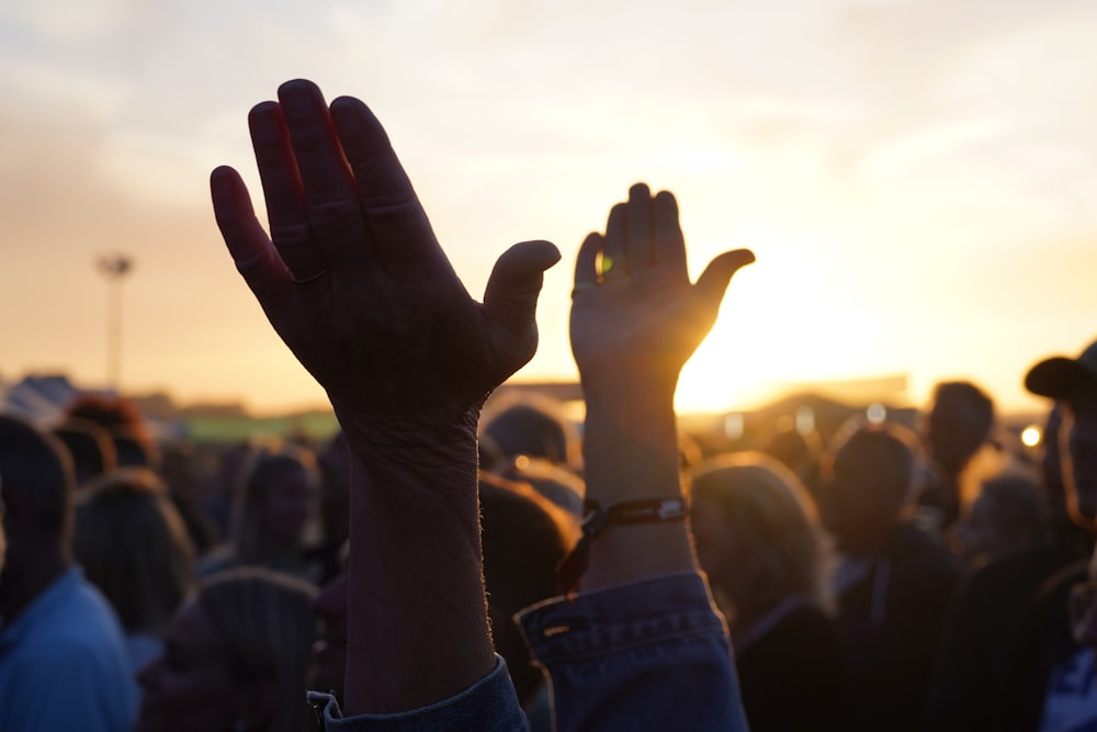 a person's hands in the air with a crowd in the back