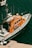 A bright orange rescue boat is moored at a dock, featuring several antennas and life-saving equipment. The boat's side is marked with the phrase 'Les sauveteurs en mer'. The surrounding water is a deep blue-green color, with another small boat visible partially in the background.