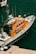 A bright orange rescue boat is moored at a dock, featuring several antennas and life-saving equipment. The boat's side is marked with the phrase 'Les sauveteurs en mer'. The surrounding water is a deep blue-green color, with another small boat visible partially in the background.