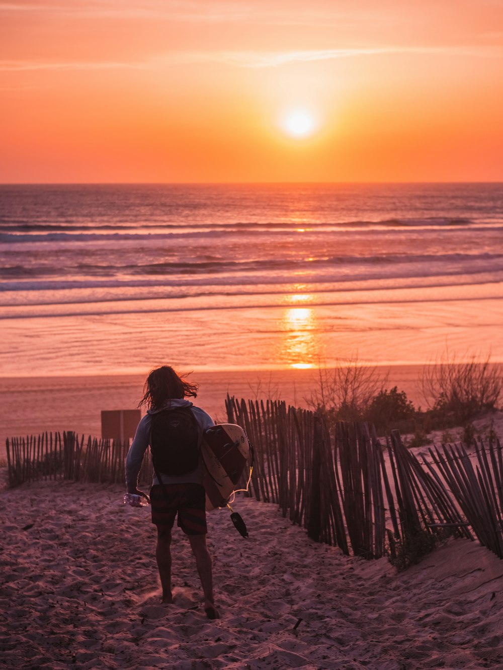 a couple of people walk down a beach holding surfboards