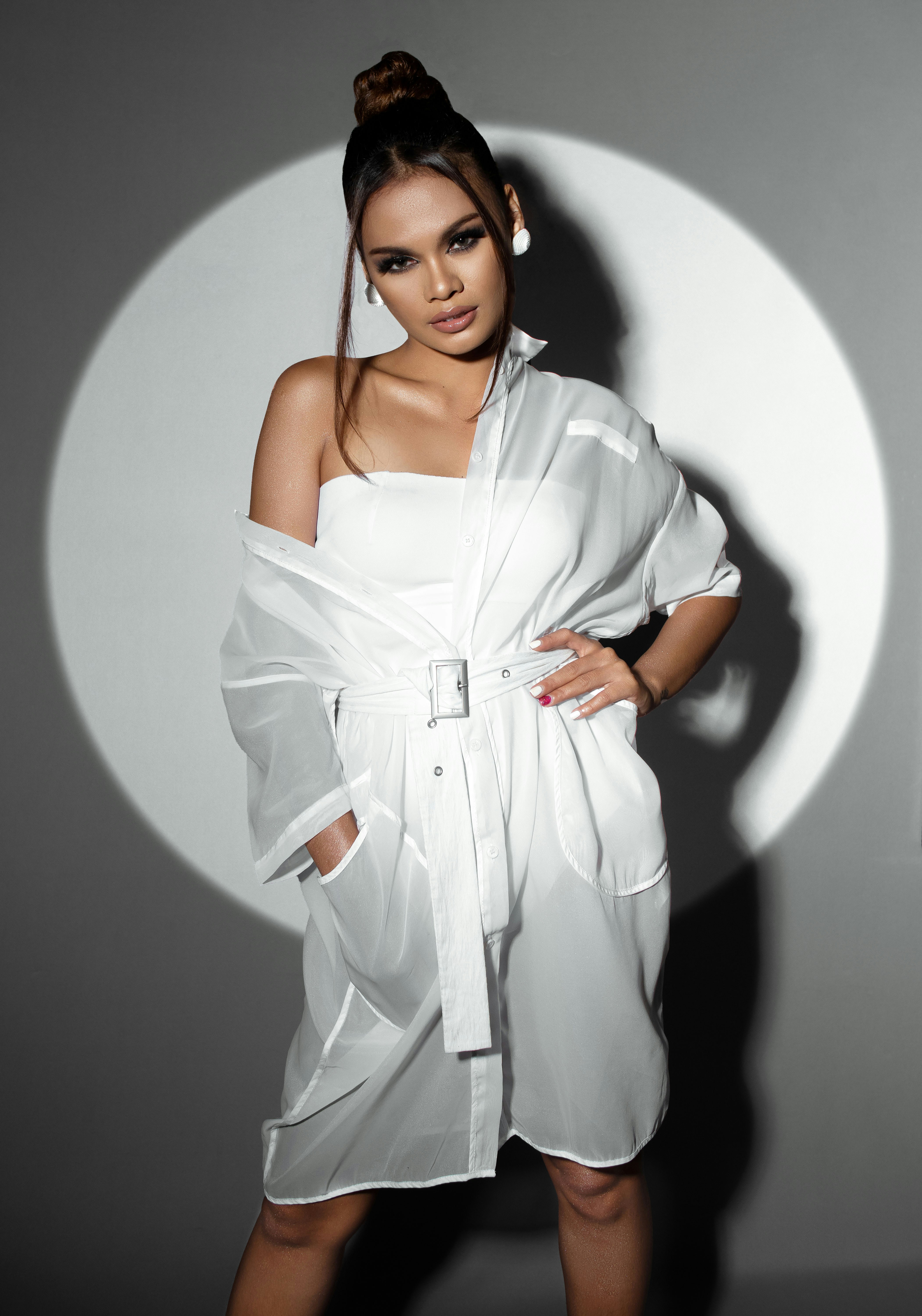 Woman in white outfit posing against a spotlight.
