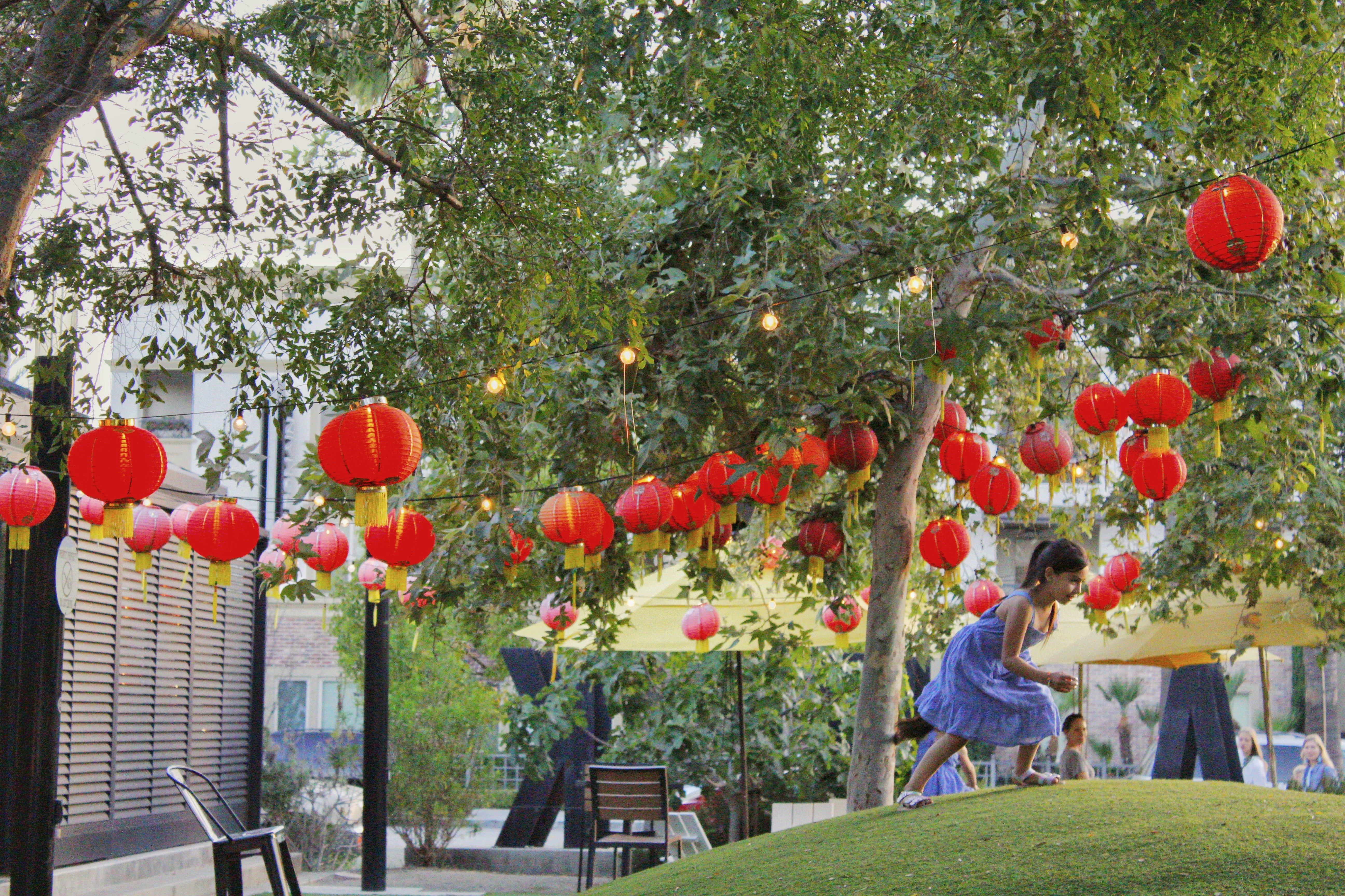 Ein Mädchen im blauen Kleid steht neben einem Baum mit roten Laternen