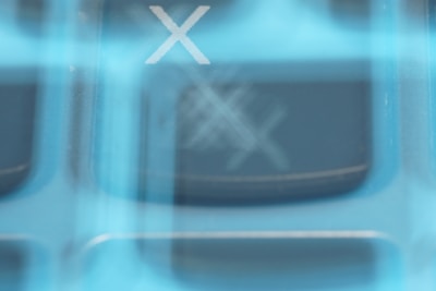 A close-up image with a prominent 'X' symbol, set against a blurry background that suggests the presence of a keyboard or keypad. The image has an abstract, layered effect with a blue color tint.