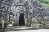 a stone building with statues with Goa Gajah in the background