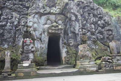 a stone building with statues with Goa Gajah in the background