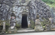 a stone building with statues with Goa Gajah in the background