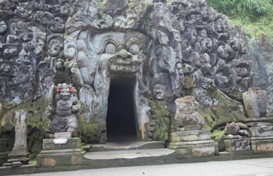 a stone building with statues with Goa Gajah in the background