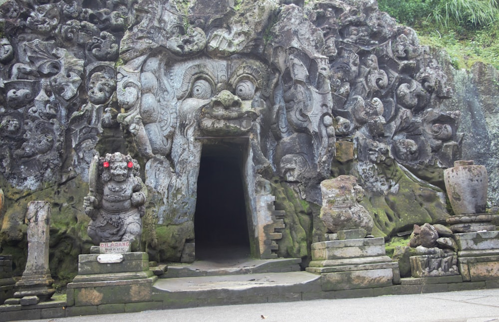 a stone building with statues with Goa Gajah in the background