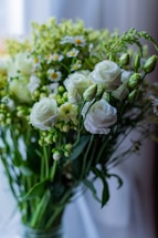 A bouquet of white roses and small daisies surrounded by green foliage, set against a softly blurred background. The flowers are in full bloom, adding a sense of freshness and elegance.