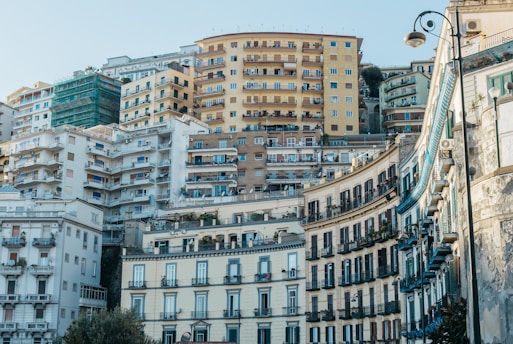 A densely built urban area with multiple layers of apartment buildings and stacked structures. The architecture varies between older, ornate buildings in the foreground and more modern, utilitarian buildings in the background. There are balconies, windows, and a street lamp visible, indicating a residential neighborhood.