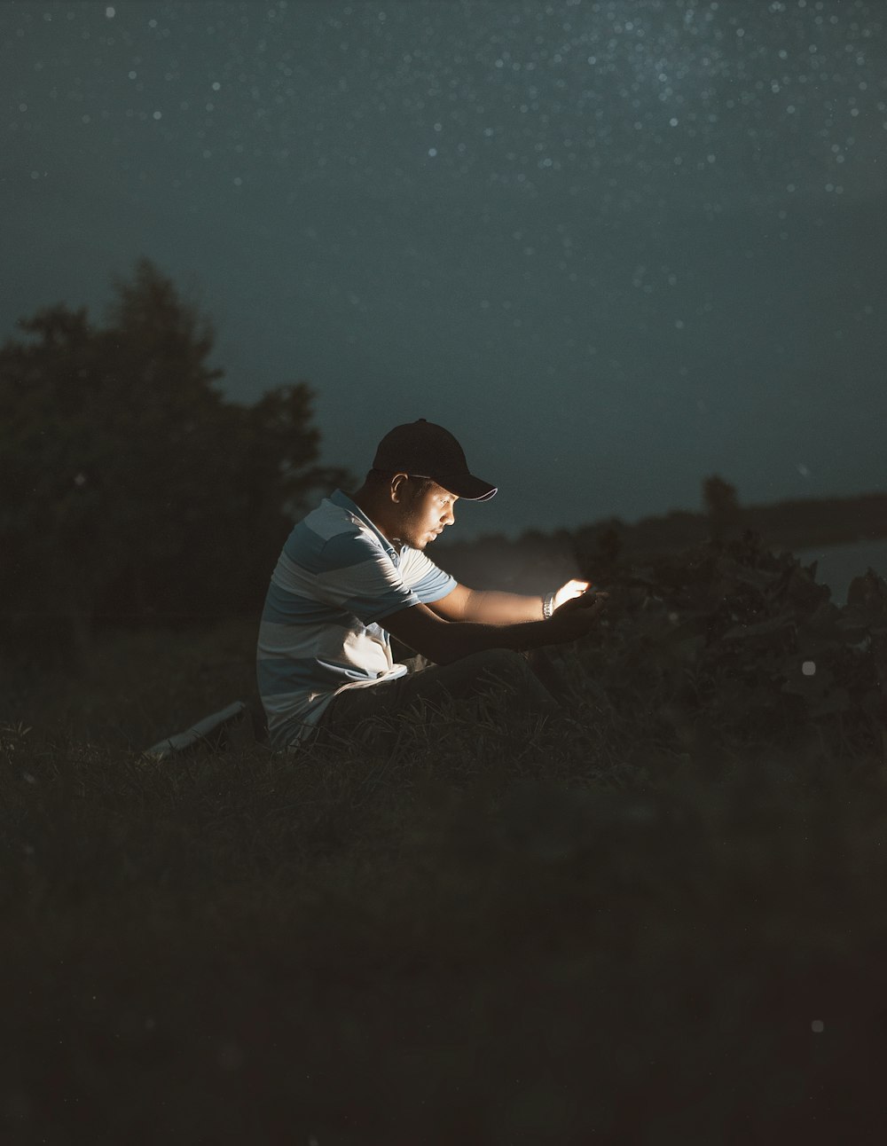 a man in a hat and shirt sitting on a hill at night