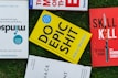 Several books placed on a grass surface, including titles like 'Mindsight,' 'Do Epic Shit,' and 'Skill Kill.' The covers of the books are visible, with varying colors including yellow, red, and blue. The books are arranged in a casual, overlapping manner.
