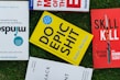Several books placed on a grass surface, including titles like 'Mindsight,' 'Do Epic Shit,' and 'Skill Kill.' The covers of the books are visible, with varying colors including yellow, red, and blue. The books are arranged in a casual, overlapping manner.