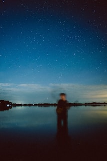 A surreal scene of a figure floating above a quiet lake under a starry night sky.