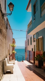 a stone walkway between buildings with a body of water in the background