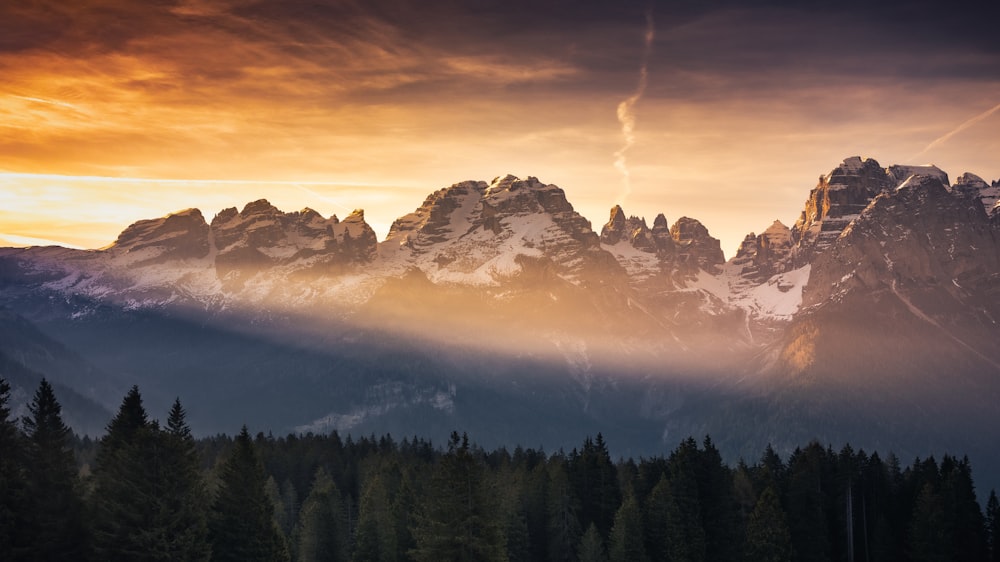 a mountain range with clouds and a rainbow in the sky