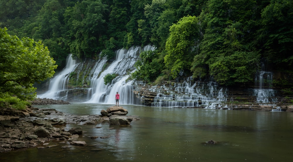 Eine Person, die auf einem Felsen vor einem Wasserfall steht