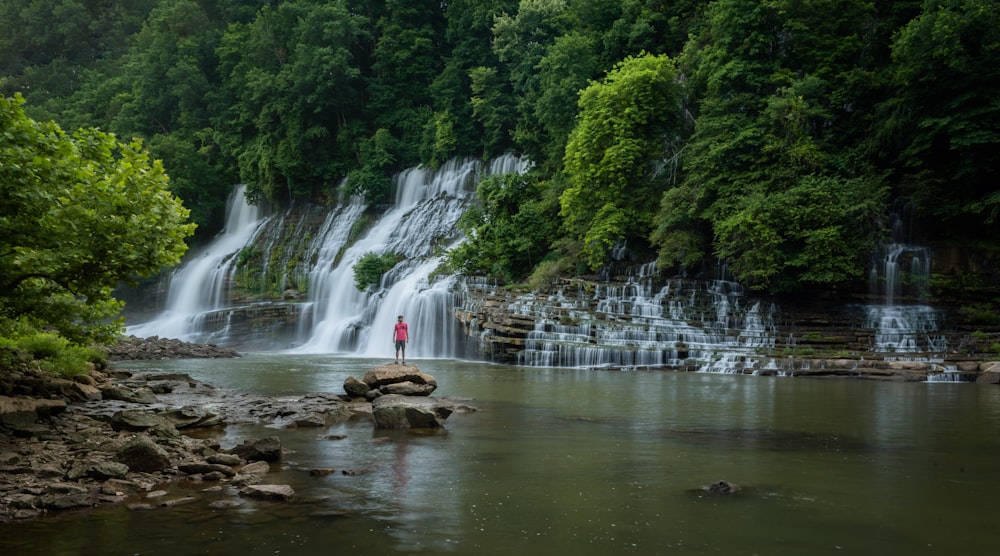 a person standing on a rock in front of a waterfall