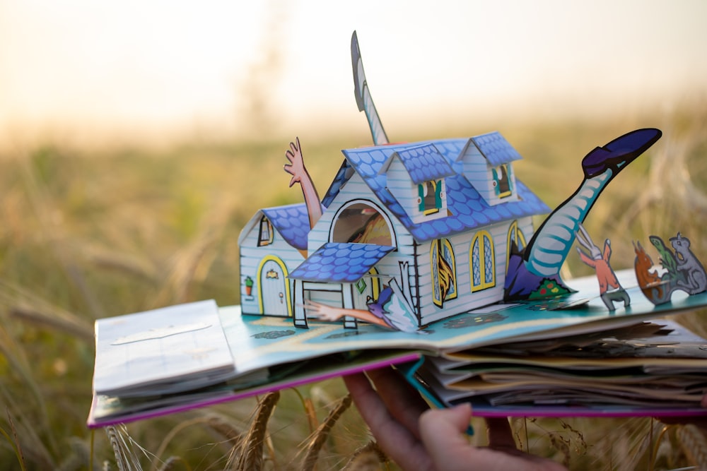 a hand holding a book with a cartoon house on it