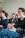 A group of people is seated in a bright room, focusing on a presentation or speaker. They appear engaged and slightly amused. The setting suggests a classroom or workshop environment. The individuals present are casually dressed and are taking notes.