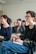 A group of people is seated in a bright room, focusing on a presentation or speaker. They appear engaged and slightly amused. The setting suggests a classroom or workshop environment. The individuals present are casually dressed and are taking notes.