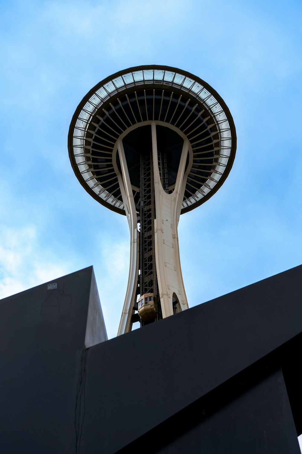 a tall tower with a circular top with Space Needle in the background