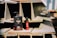 Two bottles of Maro 17 collagen shampoo and hair product are placed on a stack of industrial metal beams. The large black bottle contrasts with a smaller red bottle next to it. The scene is well-lit with natural sunlight casting shadows, highlighting the texture of the beams.